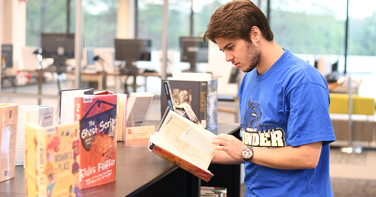 Alumnus Matthew Archambault reads through the new releases available at the Lewis Library.